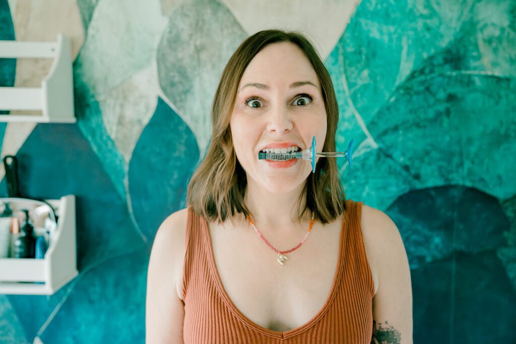 A woman makes a silly face with a botox syringe in her teeth