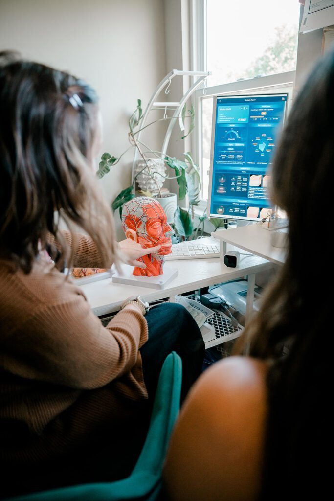 Two women sit with their backs to the camera and look at a model of the layers of human skin