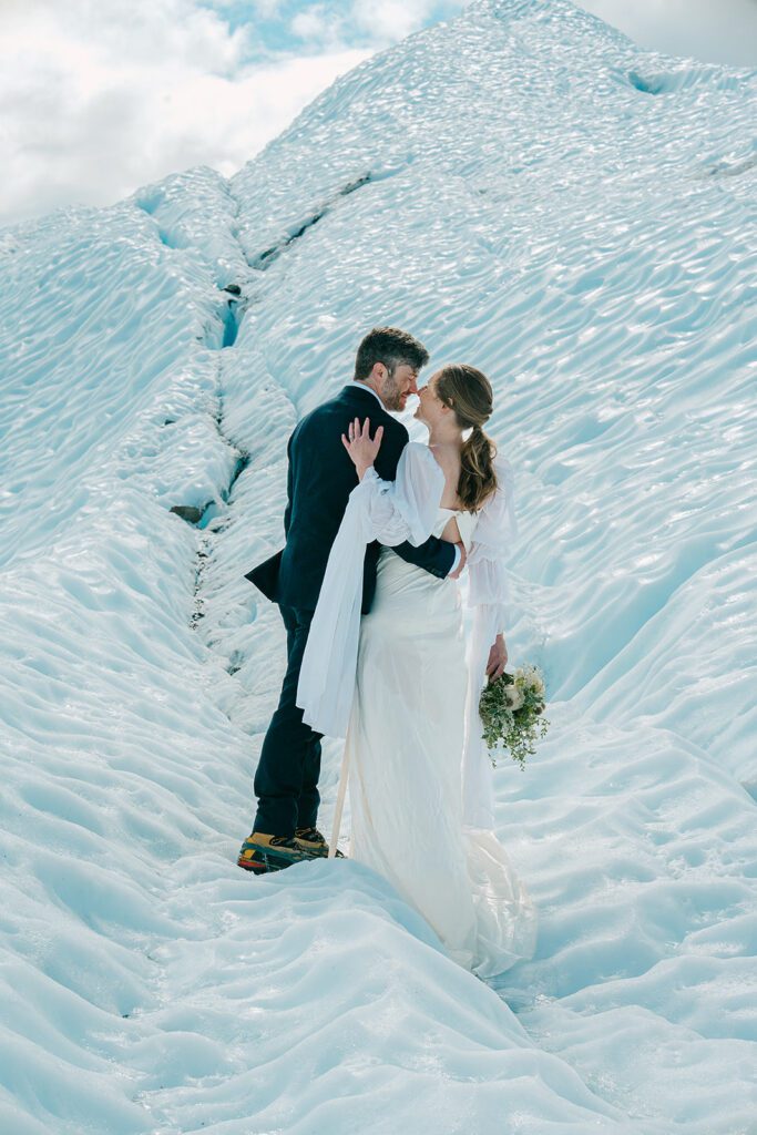 A man and woman in wedding clothes kiss atop a glacier in Alaska