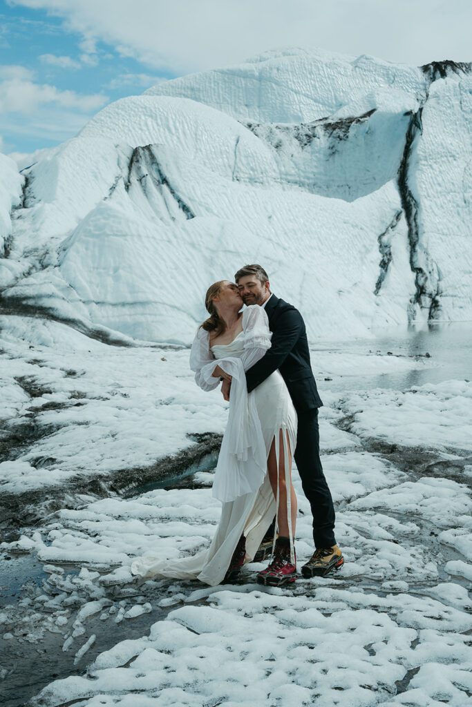 A man and woman in wedding clothing embrace on a glacier in Alaska. 