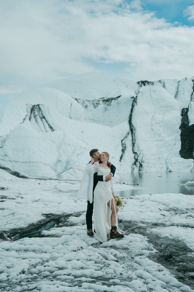 A man and woman in wedding clothing embrace on a glacier in Alaska. 