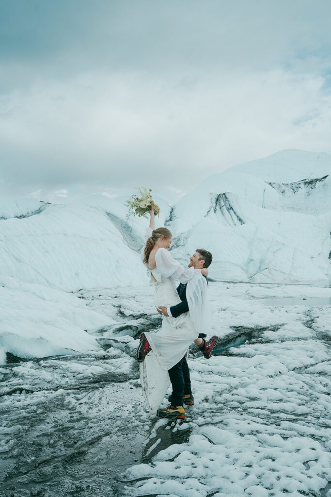 A man and woman in wedding clothing embrace on a glacier in Alaska. 