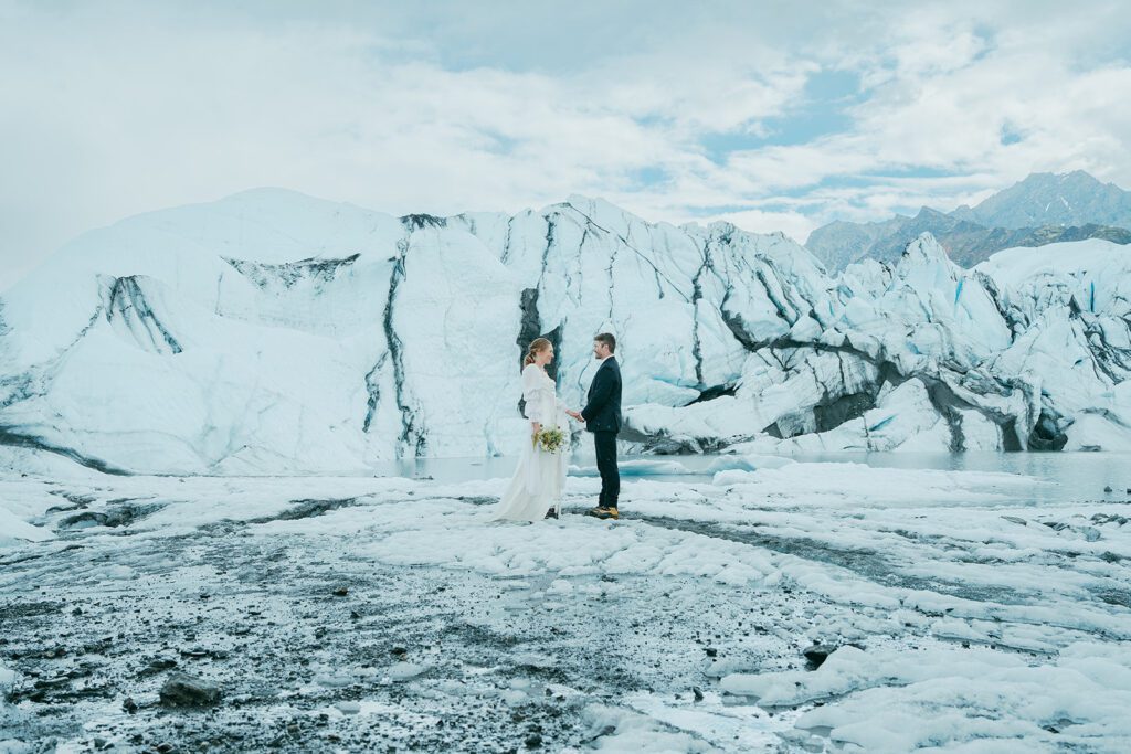 A man and woman in wedding clothing exchange wedding vows on a glacier in Alaska. 