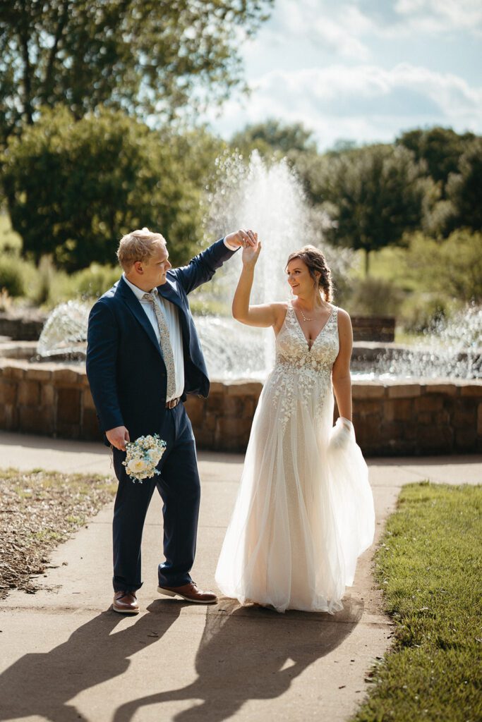 A groom twirls his bride in front of a fountain.