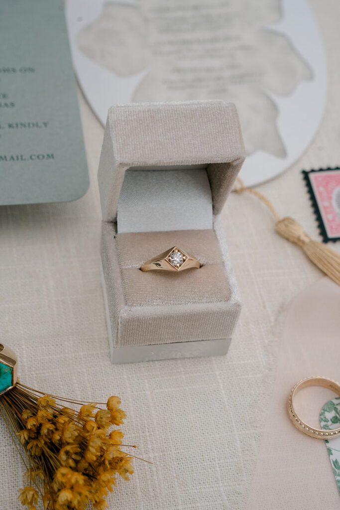 A mans wedding band with a single diamond sits in a ring box. 