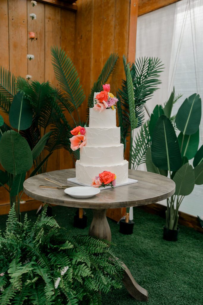 A wedding cake with hot pink flowers sits in front of greenery