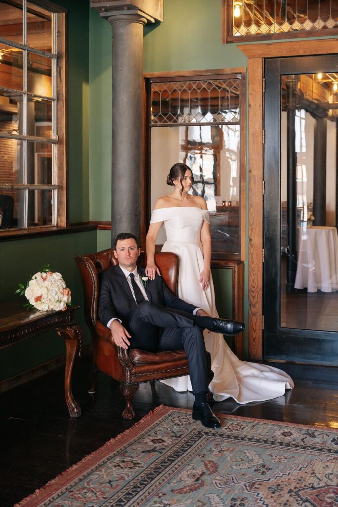 Portrait of a bride and groom indoors at a kansas city wedding venue. The groom sits in a chair.