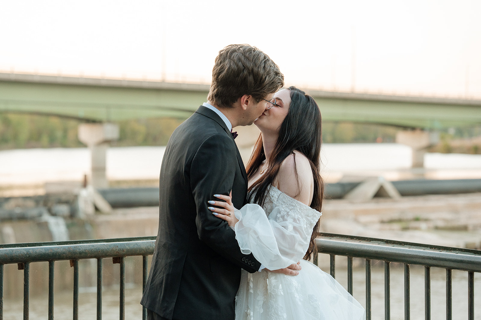 A bride and groom kiss during sunset in front of the Kansas River at Lawrence wedding venue