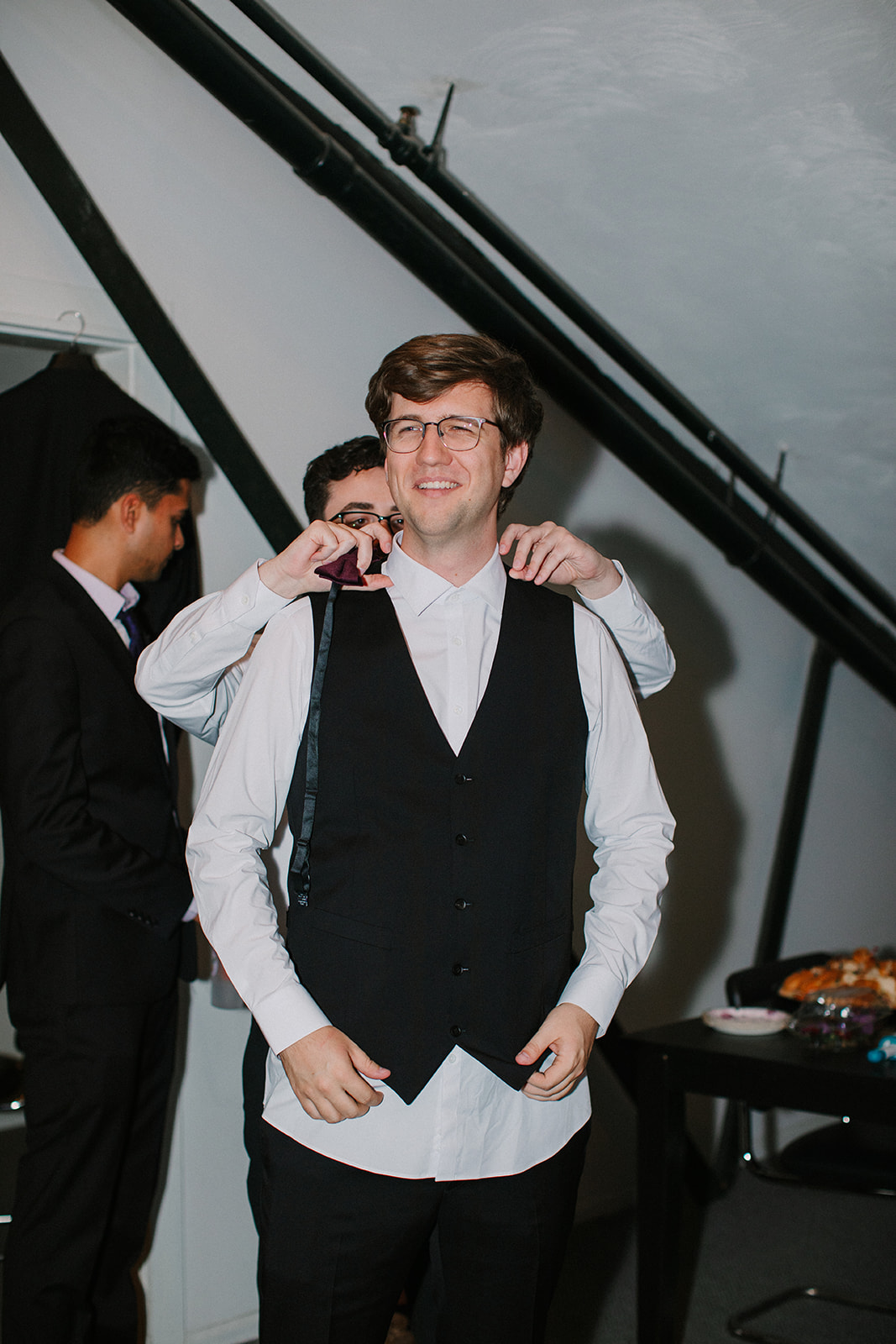 A groom has his bowtie adjusted from behind