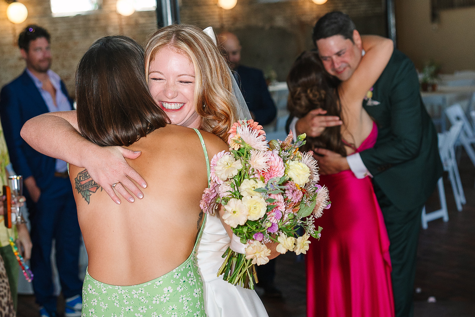 bride hugs friend while groom hugs friend in background